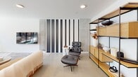Located at 1314 Spring Garden St in Philadelphia, PA, this single-floor space offers a thoughtfully designed layout that blends modern aesthetics with functional versatility. The combined dining and living area serves as the heart of the space, characterized by clean white walls, large floor-to-ceiling sliding glass doors, and oversized spherical pendant lighting that creates a warm, inviting atmosphere. The dining area features a substantial wood table surrounded by woven leather chairs, accented by striking large-scale abstract wall art that adds visual depth. The adjacent living area is understated and contemporary, with a wall-mounted flat screen and neutral furnishings that complement the refined palette throughout. Natural light flows generously through the expansive glazed doors, which open directly onto a spacious outdoor terrace enclosed by sleek metal railings. The terrace offers open views of Philadelphia's surrounding urban landscape, including classic brick architecture and the city skyline. A dedicated private room, finished with textured panel walls, a deep green ceiling, and recessed lighting, provides an intimate setting ideal for meetings or focused work. A connecting hallway ties the spaces together efficiently. The overall ambiance is polished, modern, and urban.