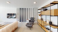 Located at 1314 Spring Garden St in Philadelphia, PA, this single-floor space offers a thoughtfully designed layout that blends modern aesthetics with functional versatility. The combined dining and living area serves as the heart of the space, characterized by clean white walls, large floor-to-ceiling sliding glass doors, and oversized spherical pendant lighting that creates a warm, inviting atmosphere. The dining area features a substantial wood table surrounded by woven leather chairs, accented by striking large-scale abstract wall art that adds visual depth. The adjacent living area is understated and contemporary, with a wall-mounted flat screen and neutral furnishings that complement the refined palette throughout. Natural light flows generously through the expansive glazed doors, which open directly onto a spacious outdoor terrace enclosed by sleek metal railings. The terrace offers open views of Philadelphia's surrounding urban landscape, including classic brick architecture and the city skyline. A dedicated private room, finished with textured panel walls, a deep green ceiling, and recessed lighting, provides an intimate setting ideal for meetings or focused work. A connecting hallway ties the spaces together efficiently. The overall ambiance is polished, modern, and urban.