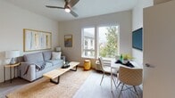 This single-floor unit is thoughtfully designed with a clean, modern aesthetic characterized by neutral tones, light-toned wood flooring, and an abundance of natural light. The open-concept layout connects the kitchen and living spaces seamlessly, creating an efficient and welcoming flow throughout.

The kitchen is outfitted with white cabinetry, light quartz countertops, stainless steel appliances including a range, microwave, and refrigerator, as well as an in-unit stacked washer and dryer. A single-basin stainless steel sink completes the functional workspace.

The living area features large windows that frame lush tree canopy views, flooding the space with natural light. A ceiling fan overhead and a wall-mounted television enhance everyday comfort, while wood-look flooring ties the space together cohesively.

The bedroom is a serene retreat, offering oversized windows with greenery views, a padded upholstered headboard wall, and warm neutral wall tones. A second bedroom, accessible from the main living space, provides flexibility and shares the same understated design language.

The bathroom features wood-look flooring, a white vanity with gold-toned hardware, and a shower-tub combination. Throughout, the space maintains a consistent, contemporary character that balances comfort with modern efficiency.