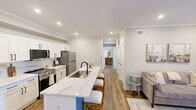 Located on Pointe Grand Way in Bethlehem, GA, this 870-square-foot single-story apartment features 2 bedrooms and 2 bathrooms, delivering a cohesive, modern aesthetic across every room. The kitchen is a standout feature, boasting white shaker-style cabinetry with matte black hardware, quartz countertops with marble-like veining, a two-toned island with seating, stainless steel appliances, and recessed lighting — all accented by crown molding. A dedicated dining area sits adjacent to the kitchen. The living room offers a comfortable, open feel with recessed lighting, crown molding, wood-look flooring, and a door providing access to the exterior. The primary bedroom measures 170 square feet and includes a walk-in closet, natural light from dual windows, and wood-look flooring. The second bedroom also features a dedicated closet and ample space. Both bathrooms are finished with white shaker vanities, quartz countertops, matte black fixtures, and wood-look flooring. The primary bath includes a lighted vanity mirror, a tall storage cabinet, and a glass-enclosed shower. Consistent warm-toned wood-look flooring and a neutral gray-white color palette unify the home's clean, contemporary style.