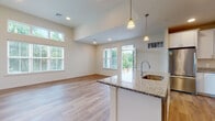 This single-floor residence is designed with an open-concept layout that connects the kitchen and living area seamlessly, creating a spacious and functional environment. The kitchen is well-appointed with white shaker-style cabinetry extending to the ceiling, granite countertops, a stainless steel refrigerator, electric range, and over-the-range microwave. A peninsula with an undermount sink and pendant lighting above provides additional workspace and serves as a natural division between the kitchen and the living area.

The living space benefits from generous natural light, delivered through multiple windows and a glass door that opens to a private balcony with outdoor views of greenery. Elevated ceilings in the main living area enhance the sense of openness, while recessed lighting adds to the bright, airy ambiance.

Wood-look plank flooring runs consistently throughout the unit. The bedroom features a walk-in closet with built-in shelving and rod storage. The en-suite bathroom includes white cabinetry, granite countertops, a dual-sink vanity, and a full-size soaking tub with a shower. An additional bathroom is also present, finished with consistent materials and a tub-shower combination.
