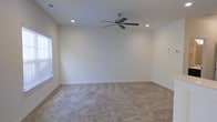 This two-floor space presents a well-maintained interior designed with simplicity and functionality in mind. The pictured room features soft, neutral-toned walls that create a bright and welcoming atmosphere, complemented by plush wall-to-wall carpeting in a warm beige tone that adds comfort underfoot. Recessed ceiling lights provide even, ambient illumination throughout the room, while a five-blade ceiling fan with a brushed nickel finish serves both aesthetic and practical purposes, promoting air circulation. A window fitted with white blinds allows natural light to filter into the space, enhancing its airy feel. Clean white baseboards frame the room neatly, contributing to the overall polished appearance. The room offers a generous, open layout with no obstructions, making it highly adaptable for a variety of uses. The understated design palette of whites and beiges throughout ensures the space feels cohesive and move-in ready. Spanning two floors, this property provides ample room for comfortable living across multiple levels, with this particular room exemplifying the clean, neutral aesthetic carried throughout the home.