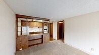 Located at 1769 Shadetree Way in Palm Springs, FL, this efficiently designed one-bedroom, one-bathroom unit offers a practical and functional single-floor layout. The combined kitchen and living area serves as the heart of the home, featuring warm-toned wood cabinetry with ample upper and lower storage, white countertops, a full suite of appliances including a refrigerator and electric range, and a built-in open shelving unit that visually separates the kitchen from the living space. The kitchen floor is finished in hardwood, while the living area transitions to neutral carpet underfoot. A textured ceiling runs throughout the unit. Natural light enters the living area through a large front-facing window, complemented by a dedicated entry area with hardwood flooring just inside the front door. The bedroom is a comfortable size, equipped with a ceiling fan and a window offering outdoor views. Three closets throughout the unit provide generous storage options. The bathroom is clean and straightforward, featuring a full tub-shower combination. A utility room off the kitchen houses the water heater, adding practical convenience. The hallway connects the main living spaces efficiently, completing this well-organized and functional home.