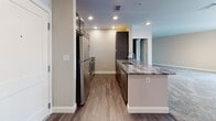 Located at 7 Elm St in Walpole, Massachusetts, this single-floor residence offers a thoughtfully designed open-concept layout with modern finishes throughout. The kitchen is a standout feature, showcasing dark wood cabinetry, striking granite countertops, stainless steel appliances including a refrigerator and range, and a breakfast bar that opens seamlessly to the living area. Recessed lighting illuminates the kitchen, while warm wood-look flooring grounds the space with a contemporary aesthetic.

The generously sized living area is finished with plush carpeting and neutral-toned walls, creating a bright and welcoming atmosphere. Large windows flood the space with natural light and provide views of the surrounding building exterior. A private balcony is accessible via a glass-paneled door, offering an outdoor retreat. Additional carpeted rooms provide flexible spaces suitable for bedrooms or a home office, each benefiting from the same clean, neutral palette.

The bathroom is well-appointed with tile flooring, a full tub-shower combination, a granite-topped vanity with dark wood cabinetry, and chrome fixtures, maintaining the consistent quality seen throughout the residence. The overall design emphasizes comfort, functionality, and modern style in a move-in-ready layout.