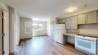 Located at 2727 Lancashire Rd in Cleveland Heights, OH, this one-bedroom, one-bathroom unit offers a thoughtfully organized single-floor layout. Light-toned hardwood-style flooring runs throughout the space, lending a clean, cohesive look to every room.

The kitchen is efficiently designed with ample gray shaker-style cabinetry lining the walls, providing generous storage. Light-toned countertops complement the cabinetry, and white appliances — including a refrigerator, range, and sink — are neatly integrated into the layout. A flush ceiling fixture provides steady overhead lighting.

The bedroom is a comfortable, well-proportioned room bathed in natural light from a wide, multi-pane window that frames views of the surrounding Cleveland Heights neighborhood, including mature tree canopy and nearby rooftops. Clean white walls and warm wood-toned flooring give the room a bright, airy feel.

The bathroom is notably spacious and accessibility-focused, featuring a roll-under vanity with drawer storage, grab bars, a handheld showerhead, and a barrier-free walk-in shower stall. Hexagonal tile flooring adds a subtle decorative touch while maintaining a neutral palette consistent with the rest of the unit.

Overall, the space presents a clean, functional, and accessible design suited for comfortable everyday living.