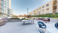 Located at 1441 Peachtree St NE in Atlanta's vibrant Midtown neighborhood, this outdoor amenity level offers a thoughtfully designed open-air retreat that blends recreation, relaxation, and social gathering in one cohesive space. The centerpiece is a expansive resort-style swimming pool with crystal-clear turquoise water, lined with modern in-pool loungers and a generous sun deck outfitted with rows of chaise lounges, inviting residents to unwind beneath the open Atlanta sky. Adjacent to the pool, a dedicated pickleball court with a bold blue surface provides a dynamic space for sport and recreation, complemented by a cornhole lawn area for casual outdoor games. A separate patio zone features a ping-pong table and stylish woven lounge chairs, creating an engaging social hub. The lounge seating area is anchored by a fire pit table surrounded by contemporary upholstered sofas and accent chairs, set atop wood-look deck flooring for a warm, inviting ambiance. Outdoor grilling stations and dining tables with red seating add a communal entertaining dimension, while raised planter beds filled with ornamental grasses and young trees provide natural texture and greenery throughout. The entire deck is framed by a lush green privacy wall and benefits from abundant natural light and open sky views.