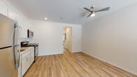 This single-floor unit offers a clean, modern aesthetic defined by light hardwood-style flooring that flows consistently throughout the space. The open-concept layout seamlessly connects the living area and kitchen, creating a cohesive and functional environment. A ceiling fan with a built-in light fixture is centrally positioned in the living area, enhancing air circulation and providing ambient lighting. Recessed lighting adds further illumination throughout.

The kitchen is well-appointed with gray shaker-style cabinetry, granite-look countertops, a stainless steel refrigerator, gas range, and microwave. A single-basin sink is conveniently situated beneath the upper cabinetry. The kitchen opens directly into the living space, making it ideal for everyday living.

The bedroom is generously sized, featuring two large windows that invite abundant natural light and offer views of surrounding greenery. A wall-mounted PTAC unit provides climate control. The bathroom maintains the same design language as the rest of the unit, with gray cabinetry, granite-look countertops, a single undermount sink, and hardwood-style flooring. A barn-style sliding door is a notable architectural detail visible in the floor plan, adding a stylish touch to the overall design.