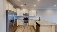 This single-floor residence in Tewksbury, Massachusetts offers a thoughtfully designed layout with modern finishes throughout. The open-concept kitchen serves as a central highlight, featuring crisp white shaker-style cabinetry extending to the ceiling, speckled granite countertops, a classic subway tile backsplash, and a full suite of stainless steel appliances including a refrigerator with ice maker, electric range, over-the-range microwave, and dishwasher. A peninsula with a undermount sink and matte black faucet provides additional prep space and casual seating potential. Recessed lighting and crown molding add a polished touch to the kitchen and adjoining living area.

The living space features warm wood-look flooring, crown molding, a ceiling fan with light, and a glass-paned exterior door that allows natural light to flow in. Bedrooms are carpeted for comfort, finished in neutral tones, and equipped with ceiling fans and window blinds offering natural light and outdoor views.

Bathrooms are well-appointed, with one featuring a framed glass walk-in shower, light tile flooring, granite vanity top, and bronze hardware accents. A second bathroom offers a granite-topped vanity and coordinating tile flooring, maintaining a consistent, refined aesthetic throughout the home.