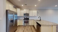 This single-floor residence in Tewksbury, Massachusetts offers a thoughtfully designed layout with modern finishes throughout. The open-concept kitchen serves as a central highlight, featuring crisp white shaker-style cabinetry extending to the ceiling, speckled granite countertops, a classic subway tile backsplash, and a full suite of stainless steel appliances including a refrigerator with ice maker, electric range, over-the-range microwave, and dishwasher. A peninsula with a undermount sink and matte black faucet provides additional prep space and casual seating potential. Recessed lighting and crown molding add a polished touch to the kitchen and adjoining living area.

The living space features warm wood-look flooring, crown molding, a ceiling fan with light, and a glass-paned exterior door that allows natural light to flow in. Bedrooms are carpeted for comfort, finished in neutral tones, and equipped with ceiling fans and window blinds offering natural light and outdoor views.

Bathrooms are well-appointed, with one featuring a framed glass walk-in shower, light tile flooring, granite vanity top, and bronze hardware accents. A second bathroom offers a granite-topped vanity and coordinating tile flooring, maintaining a consistent, refined aesthetic throughout the home.