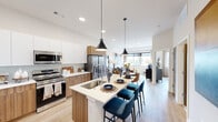 This well-appointed one-bedroom, one-bathroom residence in Aurora, Colorado, offers a thoughtfully designed single-floor layout that maximizes every inch of its efficiently proportioned footprint. The open-concept kitchen and living area serves as the heart of the home, where a central island with a white quartz countertop and bar seating anchors the space. The kitchen features stainless steel appliances, a stylish tile backsplash, and a two-tone cabinetry design combining crisp white upper cabinets with warm wood-grain lower cabinets. Pendant lighting adds a modern touch overhead. The living area benefits from generous natural light through large windows that frame outdoor views, creating a bright and welcoming atmosphere with light-toned hardwood flooring throughout. The bedroom is a calm retreat accented by vertical wood slat wall panels and direct access to a dedicated closet. The bathroom showcases a wood-toned vanity with an illuminated mirror and a tiled walk-in shower. An in-unit laundry area with a stacked washer and dryer adds everyday convenience. The overall design aesthetic is clean, contemporary, and cohesive, reflecting modern residential living in a compact yet functional arrangement.