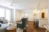 This single-floor residence combines refined architectural details with a warm, cohesive aesthetic throughout. The entryway welcomes with rich hardwood flooring, crisp white walls, and crown molding that carry through the main living areas. The living room is bright and inviting, benefiting from large windows with floor-to-ceiling drapes and a ceiling fan, creating an airy atmosphere ideal for relaxing or entertaining. Adjacent to the living room, a dedicated dining area features elegant wainscoting on the walls and track lighting overhead, lending a polished, formal character to the space. The kitchen is well-equipped with white shaker-style cabinetry, granite countertops, a classic subway tile backsplash, and a full suite of stainless steel appliances, including a refrigerator, range, and microwave. A central island provides additional prep and serving space. The bedroom is generously sized, carpeted for comfort, and offers ample natural light through a large window. A walk-in closet provides substantial storage, and a wall-mounted television is included. The bathroom is finished with a dual-sink granite vanity, white cabinetry, and a glass-enclosed shower, maintaining the home's clean and sophisticated style throughout.