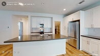 This two-floor home offers a bright, contemporary design throughout, characterized by crisp white walls, light wood-style luxury vinyl flooring, and an abundance of natural light from multiple windows fitted with blinds. The open-concept living and dining area features a ceiling fan, recessed lighting, and large sliding glass doors that fill the space with daylight. The kitchen is well-appointed with white shaker-style cabinetry, dark quartz countertops, subway tile backsplash, a large center island with an undermount sink, and stainless steel appliances including a full-size refrigerator. A pantry provides additional storage. The bedrooms offer comfortable carpeted or wood-style flooring, with windows that invite natural light. The primary bathroom is generously sized, featuring a dual-sink vanity with dark countertops, white cabinetry, and a dedicated walk-in shower with a glass door and white tile surround. A secondary bathroom mirrors this clean aesthetic with a single vanity and a tub-shower combination. A dedicated laundry room includes full-size Whirlpool washer and dryer units beneath upper white cabinetry, providing excellent utility space. Throughout, the home maintains a consistent, modern, and move-in-ready aesthetic.