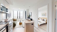 This efficiently designed one-bedroom, one-bathroom unit at 500 Upper Wellington Street in Hamilton, Ontario offers a well-organized layout across a single floor. The contemporary design is characterized by a clean, neutral palette, light wood-tone flooring throughout, and large black-framed floor-to-ceiling windows that flood the space with natural light and frame elevated views of the surrounding Hamilton cityscape and beyond.

The open-concept living area features expansive windows on a corner-facing wall, maximizing both light and views. A sliding glass door connects the living space to a private balcony, extending the usable area outdoors. The kitchen is thoughtfully designed with two-tone cabinetry combining warm wood-grain and matte finishes, light quartz countertops, stainless steel appliances, a subway tile backsplash, and a peninsula that provides additional prep and dining space.

The bedroom is a calm, light-filled retreat with its own large window and direct balcony access through a glass door, offering morning light and open views. The bathroom features large-format neutral tiles, a wood-grain vanity with an undermount sink, and a mirrored medicine cabinet. The entry corridor is clean and functional, completing this well-appointed modern unit.