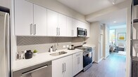 This efficiently designed single-floor unit offers a thoughtful layout encompassing a kitchen, living room, and bathroom. The modern kitchen features floor-to-ceiling white cabinetry, a herringbone-patterned tile backsplash, white quartz countertops, and a full suite of stainless steel appliances including a gas range, built-in microwave, and dishwasher. Light wood-tone flooring runs throughout, creating a cohesive and airy feel.

A corridor connects the kitchen to the living area, which is brightened by large floor-to-ceiling windows offering treetop views and abundant natural light. The living space is versatile, accommodating both a seating arrangement and a compact workspace, making it well-suited for modern living. Neutral walls provide a clean backdrop throughout.

The entryway includes a double-door closet offering practical storage, alongside a warm wood-toned entry door with a keypad lock. The bathroom is cleanly finished with a glass-enclosed walk-in shower lined in classic white subway tile, neutral stone-toned flooring, and chrome fixtures. The overall design aesthetic is contemporary and cohesive, with a neutral palette, clean lines, and modern finishes that maximize both function and comfort throughout the space.