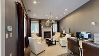 Located at 100 Park Plaza Dr in Pittsburgh, PA, this single-floor amenity space offers residents two distinct and thoughtfully designed areas. The living room exudes a warm, sophisticated ambiance with deep charcoal-gray walls, plush cream accent chairs, and a striking white-mantled fireplace as the focal point. A contemporary chandelier with cylindrical shades casts elegant lighting over the seating arrangement, while rich brown draperies frame multiple windows that invite natural light. A built-in counter area near the entrance provides a convenient workspace or refreshment station, complemented by a compact beverage refrigerator. Soaring clerestory windows above the entrance doors enhance the sense of height and openness throughout. The exercise room is a well-equipped fitness space featuring hardwood-style flooring and bright overhead panel lighting. It houses a variety of cardio and strength-training equipment, including treadmills, elliptical machines, and a multi-station cable machine, with a wall-mounted mirror that amplifies the sense of space. Together, these two spaces deliver a balanced combination of comfort and functionality, making this a versatile amenity destination for the community.
