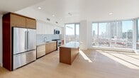 Located in the heart of downtown Los Angeles, this modern single-floor residence at 427 W 5th St offers a sleek, contemporary design with an emphasis on clean lines and bright, open living. Light hardwood flooring flows throughout the space, complementing the crisp white walls and creating a warm, cohesive aesthetic.

The open-concept kitchen is a standout feature, outfitted with stainless steel appliances including a gas range, built-in microwave, and dishwasher. Warm wood lower cabinetry is paired with white upper cabinets and a light tile backsplash, while a central island with a white countertop provides additional workspace and casual dining. Floor-to-ceiling windows flood the kitchen and adjacent living area with natural light and frame impressive views of the Los Angeles skyline.

The bedrooms continue the minimalist aesthetic with light wood flooring, large windows offering urban views, and generous closet space with built-in shelving and hanging rods. A clean entry hallway with recessed lighting provides a welcoming transition into the home.

The bathroom is well-appointed with large-format neutral tile, a combination soaking tub and shower enclosed by a frameless glass door, a wood-accented vanity with an integrated sink, an illuminated mirror, and open shelving for convenient storage. The overall design is refined, functional, and distinctly modern.