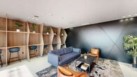 Located at 829 Garfield Ave in Jersey City, NJ, this single-floor lobby and common area space showcases a distinctly modern architectural design with a cohesive dark-toned aesthetic throughout. The entry hallway immediately sets the tone with its dramatic dark panel wall cladding, large-format light-colored tile flooring, and recessed linear LED ceiling lighting that draws the eye toward the interior. A sleek elevator is accessible directly from the entry corridor, which also features built-in cabinetry with warm wood accents, providing functional storage while adding visual warmth against the otherwise cool, contemporary palette. The hallway leads into a generously proportioned living room lounge area that serves as the heart of the space. This room is anchored by a striking feature wall adorned with a large-scale abstract mural in deep blue and gray tones, complemented by a custom dark panel entertainment wall with integrated wood-framed shelving and a centrally mounted display screen. Floor-to-ceiling windows along one wall flood the lounge with abundant natural light and offer open views of the surrounding streetscape, creating a strong indoor-outdoor connection. Large-format tile flooring continues throughout, unifying the space. The overall ambiance is polished, contemporary, and welcoming — ideal for a modern residential leasing or amenity space.