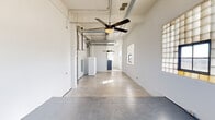 Located at 2400 S Ervay St in Dallas, TX, this 1-bedroom, 1-bathroom unit offers a distinctive industrial-loft aesthetic with thoughtful modern finishes throughout. The single-floor layout encompasses a generous combined living and dining area, a dedicated kitchen, bedroom, bathroom, closet, laundry, and hallway.

The open living and dining area immediately impresses with soaring ceilings, exposed ductwork, and polished concrete floors that run throughout the space. Ceiling fans provide comfort while adding to the loft's industrial character. Glass block windows line the walls, diffusing natural light across the expansive interior. A raised platform area within the main living space adds an architectural focal point and flexible functionality.

The kitchen features white shaker cabinetry, stainless steel appliances including a gas range and dishwasher, a modern sink with a flexible-neck faucet, and additional glass block windows that flood the room with soft, ambient light.

The bathroom offers a sleek, contemporary design with a floating vanity framed in black metal, a round mirror with stylish lighting, light wood-tone flooring, and a dark-framed glass shower door — delivering a refined contrast to the raw industrial elements found throughout the rest of the unit.

A dedicated hallway connects the private spaces, maintaining a clear separation between living and sleeping areas. The bedroom provides a comfortable, well-proportioned retreat within the overall layout.