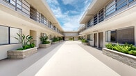 Located at 6210 Woodman Ave in the Van Nuys neighborhood of Los Angeles, this multi-unit residential building presents a classic Southern California courtyard-style design. The property is organized around a spacious, open-air central courtyard that serves as the visual and functional heart of the complex. The courtyard features a smooth, light-toned concrete floor that reflects natural sunlight, creating a bright and airy atmosphere throughout the day.

The building's two-story stucco exterior is finished in a neutral cream tone, complemented by dark-framed metal railings that line the upper-level walkways. These covered corridors provide sheltered access to individual units on both floors, with stairwells connecting the levels at the ends of the building. Unit entrances are uniformly fitted with dark doors and large windows, ensuring natural light reaches each residence.

A standout feature of the courtyard is the series of raised stone planters that run along both sides of the space, filled with a variety of lush tropical and drought-tolerant plants, including bird-of-paradise, ferns, and succulents. These green elements add a welcoming, resort-like quality to the shared outdoor space. Open to the sky above, the courtyard allows for ample sunlight and views of the characteristic blue Los Angeles sky, enhancing the overall sense of openness and California living.