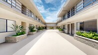 Located at 6210 Woodman Ave in the Van Nuys neighborhood of Los Angeles, this multi-unit residential building presents a classic Southern California courtyard-style design. The property is organized around a spacious, open-air central courtyard that serves as the visual and functional heart of the complex. The courtyard features a smooth, light-toned concrete floor that reflects natural sunlight, creating a bright and airy atmosphere throughout the day.

The building's two-story stucco exterior is finished in a neutral cream tone, complemented by dark-framed metal railings that line the upper-level walkways. These covered corridors provide sheltered access to individual units on both floors, with stairwells connecting the levels at the ends of the building. Unit entrances are uniformly fitted with dark doors and large windows, ensuring natural light reaches each residence.

A standout feature of the courtyard is the series of raised stone planters that run along both sides of the space, filled with a variety of lush tropical and drought-tolerant plants, including bird-of-paradise, ferns, and succulents. These green elements add a welcoming, resort-like quality to the shared outdoor space. Open to the sky above, the courtyard allows for ample sunlight and views of the characteristic blue Los Angeles sky, enhancing the overall sense of openness and California living.