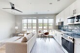 Located at 704 W Tremont Ave in Charlotte, NC's vibrant Dilworth neighborhood, this thoughtfully designed single-floor unit offers a clean, contemporary aesthetic throughout. A bright, white-walled entry hallway with recessed lighting and wood-look flooring leads into the main living area, where large, multi-pane windows flood the space with natural light and provide pleasant outdoor views of the surrounding treetops.

The open-concept layout seamlessly connects the kitchen and living room into one cohesive space. The kitchen is well-appointed with white shaker-style cabinetry, stainless steel appliances including a full-size refrigerator, electric range, and built-in microwave, complemented by a striking blue tile backsplash and light countertops with a matte black faucet. A small dining area with a round table sits adjacent to the kitchen, positioned to take full advantage of the expansive window views.

The living area features durable wood-look flooring, neutral walls, and a ceiling fan, creating a comfortable and airy atmosphere. Decorative wall art adds character throughout.

The bedroom is accessed via a stylish sliding barn door — a standout architectural detail — and offers a serene retreat with ample space and its own private bathroom. The overall design is modern and cohesive, balancing functionality with refined finishes throughout.