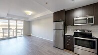 Located on the 16th floor at 140 Main St W in Hamilton, Ontario, this well-appointed unit offers a thoughtfully designed open-concept layout. Light-toned laminate flooring flows throughout the main living areas, complementing the neutral grey palette and clean architectural lines found across the space.

The kitchen is a standout feature, outfitted with rich dark espresso cabinetry extending to the ceiling, stainless steel appliances including a refrigerator, electric range, built-in microwave, and dishwasher, along with a light quartz countertop and classic tile backsplash. The kitchen opens directly onto a combined dining and living area, creating a cohesive and functional entertaining space bathed in natural light from large windows leading to the balcony.

The primary bedroom is generously sized and features floor-to-ceiling sliding glass doors that open to the balcony, allowing abundant natural light and outdoor views. A versatile den provides additional flexible space suitable for a home office or secondary sleeping area. Two full bathrooms serve the unit — one featuring a soaker tub with tiled surround, the other a tiled walk-in shower — both finished with white tile flooring, white fixtures, and clean vanities. The overall ambiance is modern, bright, and move-in ready.