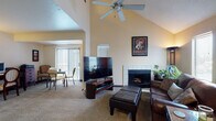 Located at 7275 N Port Washington Rd in Glendale, Wisconsin, this two-floor residence offers a thoughtfully designed layout with standout architectural details throughout. The main living area immediately impresses with dramatic vaulted ceilings and a ceiling fan overhead, creating an open, airy atmosphere. A white-tiled fireplace serves as a focal point in the living room, which features plush carpeting and access to an outdoor balcony area through sliding glass doors with vertical blinds, allowing for generous natural light. The living and dining areas flow seamlessly together, enhancing the sense of openness on the main floor. The kitchen is well-appointed with warm wood cabinetry, granite countertops, stone tile flooring, and stainless steel appliances including a refrigerator and dishwasher. A staircase with a wood-railed banister leads to the upper level, where the bedroom is tucked beneath a sloped roofline, lending it a cozy, loft-like character. The bedroom features carpeted flooring, a large closet with bifold doors, and a vanity area with granite countertops that connects to the bathroom. The bathroom is finished with tile flooring, a granite-topped wood vanity, and a shower-tub combination. Additional hallway closet space adds to the practicality of the upper level.