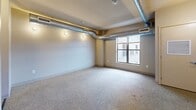 Located at 333 E Grand Ave in downtown Des Moines, Iowa, this efficiently designed studio offers a thoughtful layout across a single floor. The living area features neutral-toned carpet and exposed metallic ductwork running along the ceiling, lending the space a distinctive industrial-loft character. A window along the exterior wall brings in natural light and provides views of the surrounding urban environment.

The kitchen is compact yet fully equipped, featuring black appliances — including a full-size refrigerator, dishwasher, electric range, and microwave — paired with warm maple cabinetry, open shelving, and a dark countertop with a double-basin sink. The checkered cork-style tile flooring extends through the kitchen and into adjoining areas, adding texture and visual interest.

A dedicated closet space with built-in wire shelving provides practical storage. The bathroom continues the checkered tile flooring and includes a vanity with a dark countertop, an undermount sink, wood cabinetry, and a separate shower stall. The overall palette of neutral walls, warm wood tones, and black fixtures creates a cohesive, urban aesthetic throughout the unit.