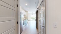 This thoughtfully designed one-bedroom, one-bathroom unit offers an efficient and modern living experience across a single floor. Light-toned luxury vinyl plank flooring runs throughout, lending a clean, cohesive aesthetic to every room.

The kitchen is a standout feature, showcasing white shaker upper cabinets paired with two-toned teal lower cabinets, a white subway tile backsplash, light quartz countertops, and a full suite of stainless steel appliances including a refrigerator, range, built-in microwave, and dishwasher. The kitchen opens directly into the dining area, creating a practical and connected layout.

The living and dining area is bright and airy, benefiting from a large sliding glass door that leads to a private balcony overlooking a lush tree canopy. A contemporary track light fixture adds a modern touch overhead.

The bedroom is a quiet, neutral space with clean white walls and the same warm flooring, offering a comfortable and versatile retreat.

The bathroom is well-appointed with white mosaic tile in the tub-shower combo, matte black fixtures, and a warm wood-toned vanity for a touch of contrast.

Throughout the unit, stylish barn-style sliding doors with matte black hardware add a distinctive architectural detail, enhancing the modern character of the space.