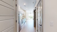 This thoughtfully designed one-bedroom, one-bathroom unit offers an efficient and modern living experience across a single floor. Light-toned luxury vinyl plank flooring runs throughout, lending a clean, cohesive aesthetic to every room.

The kitchen is a standout feature, showcasing white shaker upper cabinets paired with two-toned teal lower cabinets, a white subway tile backsplash, light quartz countertops, and a full suite of stainless steel appliances including a refrigerator, range, built-in microwave, and dishwasher. The kitchen opens directly into the dining area, creating a practical and connected layout.

The living and dining area is bright and airy, benefiting from a large sliding glass door that leads to a private balcony overlooking a lush tree canopy. A contemporary track light fixture adds a modern touch overhead.

The bedroom is a quiet, neutral space with clean white walls and the same warm flooring, offering a comfortable and versatile retreat.

The bathroom is well-appointed with white mosaic tile in the tub-shower combo, matte black fixtures, and a warm wood-toned vanity for a touch of contrast.

Throughout the unit, stylish barn-style sliding doors with matte black hardware add a distinctive architectural detail, enhancing the modern character of the space.