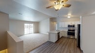 This single-floor residence offers a thoughtfully designed open-concept layout that seamlessly connects the kitchen and living area. The kitchen is a standout feature, equipped with stainless steel appliances including a refrigerator, electric range, and over-the-range microwave. Crisp white shaker-style cabinetry reaches toward the ceiling, complemented by light speckled stone countertops and a peninsula with a sink that serves as a natural divider between the kitchen and living space. Durable wood-look plank flooring runs throughout the kitchen and entry areas, transitioning to plush carpet in the spacious living room and bedrooms. The living area benefits from vaulted ceilings, a ceiling fan with a light fixture, and a sliding glass door that allows natural light to pour in. The bedrooms are comfortably sized, each featuring carpet flooring, ceiling fans, natural light from windows, and ample closet space. Two bathrooms mirror the home's clean aesthetic, with white cabinetry, stone-topped vanities, wood-look flooring, and one featuring a walk-in shower stall. Neutral wall tones and consistent finishes throughout create a cohesive, move-in ready atmosphere.