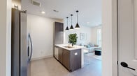Located at 2005 Brook Rd in Richmond, VA, this modern one-bedroom, one-bathroom residence offers a thoughtfully designed single-floor layout with a clean, contemporary aesthetic. The open-concept living and kitchen area serves as the heart of the home, where rich dark wood cabinetry contrasts beautifully with crisp white quartz countertops. A central kitchen island with an integrated sink and seating for multiple bar stools anchors the space, illuminated by a trio of striking matte black pendant lights. The kitchen is fully equipped with stainless steel appliances, including a side-by-side refrigerator, electric range, built-in microwave, and dishwasher, complemented by a classic subway tile backsplash. The living area flows naturally from the kitchen, featuring large sliding glass doors that invite natural light and provide direct outdoor views. The spacious bedroom offers plush carpeting, a generous window with neighborhood views, and access to a dedicated closet. The full bathroom maintains the home's modern palette with a wood-toned vanity, white quartz countertop, matte black fixtures, and a tub-shower combination. Neutral tones, recessed lighting, and clean architectural lines unify each space, creating a cohesive and comfortable living environment.