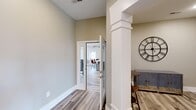 Located at 112 Mountain Flat Dr NE in Huntsville, Alabama, this single-floor community space is thoughtfully designed to provide a welcoming and functional gathering environment. The layout encompasses several distinct areas that flow seamlessly into one another, all unified by light-toned wood-look flooring and a neutral warm-gray color palette throughout.

The central lounge area serves as the heart of the space, anchored by a striking floor-to-ceiling stone fireplace with an integrated TV mount above the mantle. Vaulted ceilings and an abundance of large windows flood the room with natural light, creating an open and airy atmosphere. Comfortable seating arrangements invite relaxation and socializing.

Adjacent to the lounge is a bright game room featuring a shuffleboard table, vaulted ceilings with a ceiling fan, and expansive windows that further enhance the sense of openness. A dedicated dining area with a dark wood table and leather-upholstered seating is positioned near a glass-panel door, connecting the interior to additional areas of the building.

The kitchenette is outfitted with dark espresso cabinetry, granite countertops, a large bar-height peninsula with bar seating, pendant lighting, and essential appliances, making it ideal for catered events or casual gatherings. Decorative columns and architectural trim details add a refined touch throughout the space.