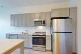 This well-appointed one-bedroom, one-bathroom residence at 950 S George Mason Drive in Arlington, Virginia offers a thoughtfully designed single-floor layout. Light hardwood-style flooring runs throughout the living areas, creating a warm, cohesive aesthetic.

The combined kitchen and dining area serves as a central hub of the home. The kitchen is outfitted with stainless steel appliances — including a refrigerator, electric range, and built-in microwave — complemented by grey shaker-style cabinetry, light quartz countertops, and a classic white subway tile backsplash. A dedicated dining space flows naturally from the kitchen, making everyday living and entertaining convenient.

The living room receives generous natural light through large windows with views of surrounding greenery. The spacious bedroom also features oversized windows fitted with horizontal blinds, allowing for adjustable natural light and outdoor views. Multiple closets throughout the unit provide ample storage.

The bathroom is finished with large-format porcelain tile flooring, a subway-tiled tub/shower surround with a curved curtain rod, and a vanity with modern hardware. In-unit laundry adds to the home's practicality. The entrance hallway provides a welcoming transition into the open, light-filled interior of this efficiently laid-out Arlington residence.