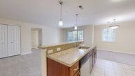 This generously sized 1-bedroom, 1-bathroom apartment offers 3,280 square feet of single-floor living space with a functional and well-appointed layout. The open-concept kitchen and living room serve as the heart of the unit, where a large kitchen island with granite-look countertops and pendant lighting anchors the space. The kitchen is equipped with rich wood cabinetry, stainless steel appliances including a refrigerator, microwave, and range. The adjoining living area features neutral carpet flooring and large sliding glass doors that flood the room with natural light and provide direct access to the private balcony, which overlooks a tree-lined community courtyard. The bedroom, spanning 180 square feet, is carpeted and includes a ceiling fan, a double-door closet, and multiple windows that bring in additional natural light. A dedicated walk-in closet area with wire shelving offers ample storage. The bathroom features a full tub/shower combo with beige tile surround and tile flooring. A separate laundry area accommodates a stacked washer and dryer unit. Warm cream-toned walls and consistent neutral finishes throughout give the apartment a cohesive and inviting ambiance.