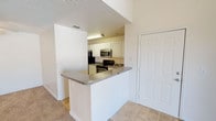 This single-floor residence offers a practical and comfortable layout designed for everyday living. The kitchen serves as a central highlight, featuring crisp white cabinetry that extends to the upper walls, providing generous storage space. A peninsula-style breakfast bar with a granite-look countertop creates a natural division between the kitchen and the adjoining living area, making it ideal for casual dining or meal prep. The kitchen is fully equipped with stainless steel appliances, including a microwave and range, as well as a black refrigerator, offering a sleek contrast to the white cabinetry. Tile flooring runs throughout the kitchen and entry areas, offering durability and easy maintenance, while plush carpeting in the living space adds warmth and comfort underfoot. A textured ceiling adds subtle architectural character to the space. The entry area features a full-panel door, providing a welcoming and secure entryway. Neutral tones throughout the space create a clean, versatile backdrop that is easy to personalize. Overall, the layout is functional and efficient, making thoughtful use of the available space while maintaining an open and airy feel.