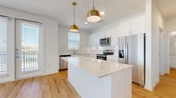 This well-appointed single-story home offers a thoughtfully designed layout across two bedrooms, two bathrooms, a combined kitchen and living area, two closets, and a dedicated laundry room. The open-concept kitchen is a standout feature, boasting crisp white shaker cabinetry, a large central island with a quartz countertop, stainless steel appliances including a refrigerator, range, microwave, and dishwasher, and striking gold pendant lights that add a warm, contemporary accent. Light wood-look flooring flows throughout the main living areas, complementing the clean, neutral color palette and creating a bright, airy atmosphere. A wide hallway connects the kitchen to the rest of the home seamlessly. The primary bedroom is generously sized, featuring light wood flooring, a ceiling fan, and multiple windows that allow natural light to fill the space. Its en-suite bathroom includes a white vanity with quartz countertops and direct access to a walk-in closet with built-in shelving. The second bedroom is carpeted, equipped with a ceiling fan, and benefits from natural light through a window. Both bedrooms offer comfortable proportions and ample storage. The dedicated laundry room houses a full-size washer and dryer. This home combines functional design with modern finishes for comfortable, move-in-ready living.