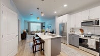 Located at 9398 Station St in Lone Tree, CO, this one-bedroom, one-bathroom residence offers a well-designed single-floor layout that maximizes every square foot of its comfortable footprint. Light wood-style flooring runs throughout, lending warmth and continuity to the open-concept living spaces.

The living room is bright and inviting, featuring large windows that fill the space with natural light and offer views of the surrounding area. The area flows seamlessly into the combined dining and kitchen space, which is outfitted with crisp white cabinetry, stainless steel appliances, a tile backsplash, and a center island with pendant lighting above — ideal for both meal prep and casual dining.

The bedroom provides a quiet retreat with a ceiling fan, sliding glass doors that open to a private outdoor patio with exterior views, and direct access to two closets for ample storage. The bathroom is clean and modern, featuring a dual-sink white vanity with generous counter space, a large mirror, and a full shower-tub combination.

Completing the layout is an in-unit laundry area, adding everyday convenience. The overall aesthetic is contemporary and cohesive, with neutral tones and quality finishes throughout that create a calm, functional living environment.