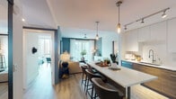 This contemporary single-floor residence is designed with a cohesive modern aesthetic, characterized by light wood flooring, bold teal and deep navy accent walls, and an open, flowing layout. The kitchen is a standout feature, offering two-tone cabinetry combining white upper cabinets with warm wood-finish lowers, stainless steel appliances, a full-size side-by-side refrigerator, and a large white waterfall-edge island with bar seating — ideal for both cooking and casual dining. Pendant lighting adds a refined touch overhead.

The living area flows seamlessly from the kitchen and is anchored by a ceiling fan, a sleek media console, and a sliding glass door that opens to a private balcony with expansive city skyline views. Natural light pours in, enhancing the airy atmosphere.

The primary bedroom features floor-to-ceiling windows with urban views, a teal accent wall, curated artwork, and access to a walk-in closet. The en-suite bathroom presents a dark dramatic accent wall, a wood-vanity with white countertop, and wood-look tile flooring. A second bedroom offers cityscape views and warm natural light. The second bathroom includes a soaking tub, a wood-finish vanity, and clean white tile finishes throughout.