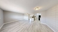 This 2-bedroom, 1-bathroom unit is laid out on a single floor, offering a practical and functional living space. Light wood-style laminate flooring runs consistently throughout the unit, creating a cohesive and clean aesthetic across all rooms.

The combined kitchen and living area forms the heart of the unit. The galley-style kitchen features white cabinetry, black appliances including a gas range and refrigerator, tile countertops, and a textured ceiling with overhead lighting. The adjacent living room is bright and open, benefiting from a window that brings in natural light and neutral gray wall tones.

The primary bedroom is a well-sized room with a ceiling fan, a window overlooking the exterior, and mirrored sliding closet doors with gold-tone frames that add a touch of character. The second bedroom is a more compact space with light gray walls, white baseboards, and the same wood-style flooring, offering a clean and versatile room.

The bathroom features warm-toned floor and wainscot tile, white upper walls, and a tub-shower combination with classic white subway tile surround. The overall ambiance of the unit is simple, clean, and move-in ready, with a neutral palette throughout that accommodates a variety of furnishing styles.