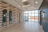 This thoughtfully designed single-floor space makes an immediate impression through its bold, artistic identity. A standout feature is the dramatic hand-painted mural that spans entire walls, showcasing sweeping horizontal brushstrokes in dark brown and white that lend the space a gallery-like character. Complementing this artwork are a set of tall, arch-framed mirrors with sleek black borders, adding depth and visual interest to the corridor area.

The flooring throughout is light-toned hardwood, contributing to a clean, airy atmosphere. Recessed lighting in the ceiling provides warm, even illumination, while large windows allow abundant natural light to pour in, offering views of the surrounding urban neighborhood.

A dedicated elevator lobby features refined vertical slat paneling in a muted steel blue, housing a stainless steel elevator and rounded wall sconces that add a modern, polished touch. This area also includes a fire safety station and building information panels, underscoring the space's practical functionality.

One of the most notable features is access to a private outdoor deck, reachable through full-height glass doors. The deck is finished with wood tile decking and warm-toned slatted railings, offering an open-air extension of the space with panoramic views of the surrounding cityscape. Overall, the space blends artistic design with functional, modern architecture.