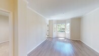 This single-floor residence offers a thoughtfully designed open-concept layout that seamlessly connects its key living areas. The kitchen is a functional highlight, featuring rich dark-toned cabinetry, stainless steel appliances including a gas range, built-in microwave, dishwasher, and refrigerator, complemented by light quartz countertops and a peninsula that opens to the dining and living areas. Crown molding adds an elegant finishing touch to the main living space, which is bathed in natural light streaming through a curved bay window framing views of lush greenery outside. Hardwood-style flooring runs throughout the main areas, while a carpeted bedroom offers direct outdoor access through a glass door with a sidelight window. A well-lit hallway with a drum pendant light connects the rooms, with a thermostat conveniently positioned near the entry. The bathrooms are finished with dark-topped vanities, white cabinetry, large mirrors, and full tub-shower combinations with curved curtain rods. The overall ambiance is clean, bright, and contemporary, with a neutral warm palette of cream and white tones creating an inviting and versatile living environment throughout.