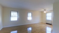 This single-floor residence offers a clean, well-maintained interior that combines classic design with comfortable, functional living. The main living area is a standout feature, showcasing polished hardwood floors that reflect natural light beautifully, creating a warm and inviting atmosphere throughout the space. Multiple double-hung windows line the walls, flooding the room with abundant daylight while offering views of the surrounding greenery outside. The neutral, cream-toned walls provide a versatile backdrop, complementing the natural wood tones of the flooring and lending the space a bright, airy feel. A classic ceiling fan with a light fixture is centrally positioned, ensuring both comfort and illumination. Clean white baseboards and trim add a crisp, finished look to the interior. The open layout of the living area allows for flexible furniture arrangements and a generous sense of space, making it well-suited for both relaxed everyday living and entertaining. The overall ambiance of the home is calm and understated, with an emphasis on natural light, clean lines, and timeless finishes that provide a solid foundation for personalization.