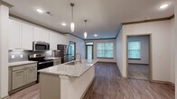 Located at 114 SE Douglas St in Lee's Summit, Missouri, this single-story residence offers a thoughtfully designed open-concept layout with modern finishes throughout. The kitchen serves as a central focal point, featuring a large granite-topped island with an undermount sink, white shaker-style cabinetry, a subway tile backsplash, and stainless steel appliances including a range, microwave, and refrigerator. Pendant lighting above the island adds a polished touch, while crown molding and recessed lighting elevate the overall aesthetic. Wood-style plank flooring extends through the main living and kitchen areas, creating a cohesive, contemporary feel.

The living area benefits from multiple windows dressed with horizontal blinds, filling the space with natural light. A separate room with a glass-panel door provides access to an outdoor area. The bedrooms are carpeted for comfort and include windows that invite additional natural light. The primary bathroom is well-appointed with a granite double-vanity, sage-toned cabinetry, a glass-enclosed walk-in shower with marble-style tile, and direct access to a walk-in closet. A secondary bathroom mirrors the same granite vanity and quality cabinetry. Throughout, the unit maintains a clean, neutral palette with consistent architectural detailing.