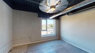 Located at 235 Virginia St in Mount Airy, NC, this single-floor unit showcases a compelling blend of industrial and modern design elements. The space is defined by its exposed ceiling ductwork and dark-painted ceiling structure, which contrast sharply with the neutral-toned walls to create a distinctive urban aesthetic. Polished concrete floors run throughout, providing a durable and visually cohesive foundation across all areas.

The main living areas feature windows that offer views of the surrounding streetscape, allowing natural light to fill the space. Ceiling fans with integrated lighting provide both comfort and illumination. The open layout lends itself to flexible use, with one area revealing built-in closet shelving and organizational features behind white panel doors.

The kitchen is efficiently designed in a galley configuration, outfitted with dark espresso cabinetry, granite-style countertops, a tile backsplash, and stainless steel appliances including an electric range and microwave. The bathroom includes a full tub-shower combination, a dark wood vanity with a granite-topped sink, and recessed lighting, maintaining the consistent design language found throughout the unit.
