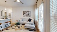 Located at 5900 S Congress Ave in Austin, TX, this well-appointed 2-bedroom, 2-bathroom residence offers a thoughtfully designed single-level layout with a clean, contemporary aesthetic throughout. Light wood-tone flooring flows seamlessly across the entire unit, complementing the bright white walls and modern finishes.

The open-concept kitchen is a standout feature, equipped with stainless steel appliances including a French door refrigerator, electric range, built-in microwave, and dishwasher. Two-tone cabinetry — white uppers and warm wood-grain lowers — pairs with light quartz countertops and a subway tile backsplash. A peninsula with a sink connects the kitchen to the combined dining and living area, which is filled with natural light from large windows and a glass door leading to an outdoor space.

The living area features a ceiling fan and generous window coverage with blinds and curtains, creating a bright, airy atmosphere. The primary bedroom offers a comfortable retreat with a large window, light wood flooring, and a dedicated closet. The second bedroom is equally well-lit and functional. Both bathrooms are finished with warm wood-tone vanities, framed mirrors, and light flooring. A dedicated laundry area and utility room add everyday convenience to this efficiently designed Austin residence.