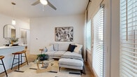 Located at 5900 S Congress Ave in Austin, TX, this well-appointed 2-bedroom, 2-bathroom residence offers a thoughtfully designed single-level layout with a clean, contemporary aesthetic throughout. Light wood-tone flooring flows seamlessly across the entire unit, complementing the bright white walls and modern finishes.

The open-concept kitchen is a standout feature, equipped with stainless steel appliances including a French door refrigerator, electric range, built-in microwave, and dishwasher. Two-tone cabinetry — white uppers and warm wood-grain lowers — pairs with light quartz countertops and a subway tile backsplash. A peninsula with a sink connects the kitchen to the combined dining and living area, which is filled with natural light from large windows and a glass door leading to an outdoor space.

The living area features a ceiling fan and generous window coverage with blinds and curtains, creating a bright, airy atmosphere. The primary bedroom offers a comfortable retreat with a large window, light wood flooring, and a dedicated closet. The second bedroom is equally well-lit and functional. Both bathrooms are finished with warm wood-tone vanities, framed mirrors, and light flooring. A dedicated laundry area and utility room add everyday convenience to this efficiently designed Austin residence.