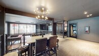 Located at 50 S Grant Ave in the heart of downtown Columbus, Ohio, this thoughtfully designed commercial space blends modern sophistication with functional versatility. The layout centers around an open-plan area anchored by a striking Sputnik-style chandelier in brushed gold, which illuminates a high-top communal table surrounded by richly upholstered leather chairs — a refined focal point for collaboration or casual gatherings.

A series of glass-enclosed private meeting rooms line one side of the floor, framed by sleek dark metal partitions that offer visual transparency while maintaining acoustic separation. Each room is appointed with its own lighting and distinctive accent walls, providing an intimate yet professional setting.

The space opens onto a mezzanine-level overlook with dark wood beam accents and metal cable railings, offering views down to a lower level that features bold red seating and patterned flooring. Large perimeter windows allow abundant natural light to filter throughout, enhancing the urban views of the surrounding downtown streetscape.

A white subway tile-clad elevator lobby and adjacent restroom corridor add a clean, architectural contrast to the warmer tones found elsewhere. Textured neutral carpeting runs throughout, tying together the varied zones with cohesion. The overall ambiance is polished and contemporary, well-suited for a dynamic professional environment.