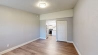 Located at 15300 W Colonial Dr in Winter Garden, Florida, this efficiently laid-out unit offers a thoughtful use of space across a single floor. The living area features warm wood-look luxury vinyl plank flooring, soft neutral gray walls, and a textured ceiling, creating a clean and contemporary ambiance. A wall-mounted HVAC unit and a window with blinds provide both climate control and natural light, with a pleasant outdoor view of greenery. The open-plan layout connects the living area directly to the kitchen, which is outfitted with white shaker-style cabinetry, stainless steel appliances including a refrigerator and electric range, an under-cabinet range hood, and a single-basin sink. Light-toned countertops and a skylight-style ceiling fixture in the kitchen add brightness to the space. A dedicated closet with paneled double doors offers practical storage. The bathroom is finished with a white vanity, coordinating hardware in brushed nickel, and wood-look flooring that ties the space together cohesively. Clean white trim and baseboards throughout contribute to the crisp, move-in-ready feel of this well-appointed unit in Winter Garden.