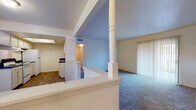This single-floor residential unit offers a functional and comfortable layout designed for everyday living. The open-concept living area is anchored by soft carpeting and a sliding glass door fitted with vertical blinds, allowing natural light to fill the room while providing access to an outdoor space. A decorative column and half-wall partition define the transition between the living area and the kitchen, adding a subtle architectural detail to the floor plan.

The kitchen is well-appointed with white cabinetry, dark granite-style countertops, a full suite of white appliances including a range and refrigerator, and durable wood-look flooring. A skylight-style ceiling fixture brightens the galley-style layout, which also features a sink along the opposing wall for added convenience.

The bedrooms are carpeted and generously sized, each equipped with a ceiling fan and light fixture. Windows in each room invite natural light and offer views of the surrounding neighborhood. The unit includes two full bathrooms, both featuring wood-look flooring, white tile tub-shower surrounds, and clean, neutral finishes throughout. The overall aesthetic is bright and neutral, providing a versatile canvas well-suited to a variety of furnishing styles.
